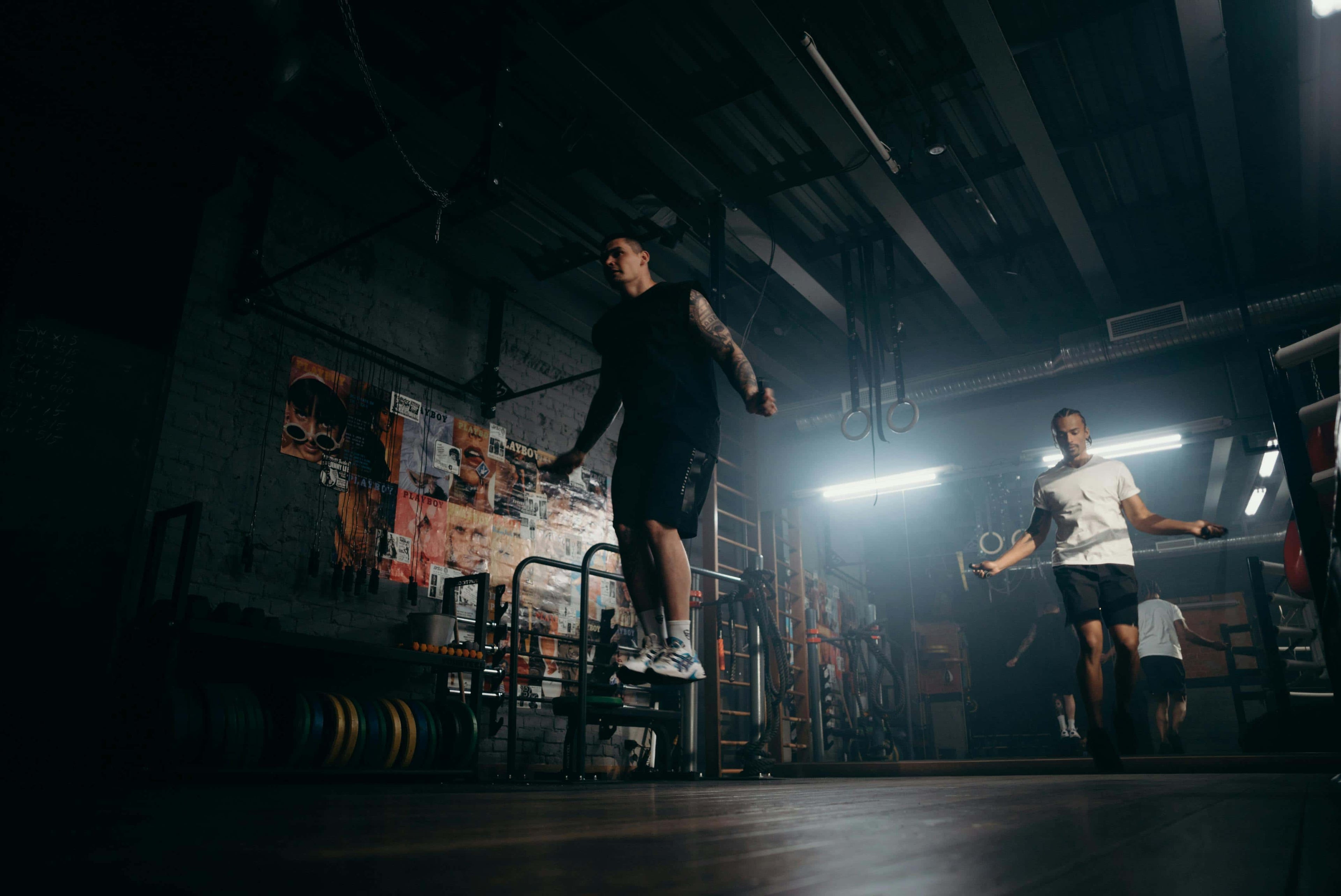 Sporters in industriële gymomgeving bezig met springtouwen; focus op kracht, coördinatie en intensieve training.